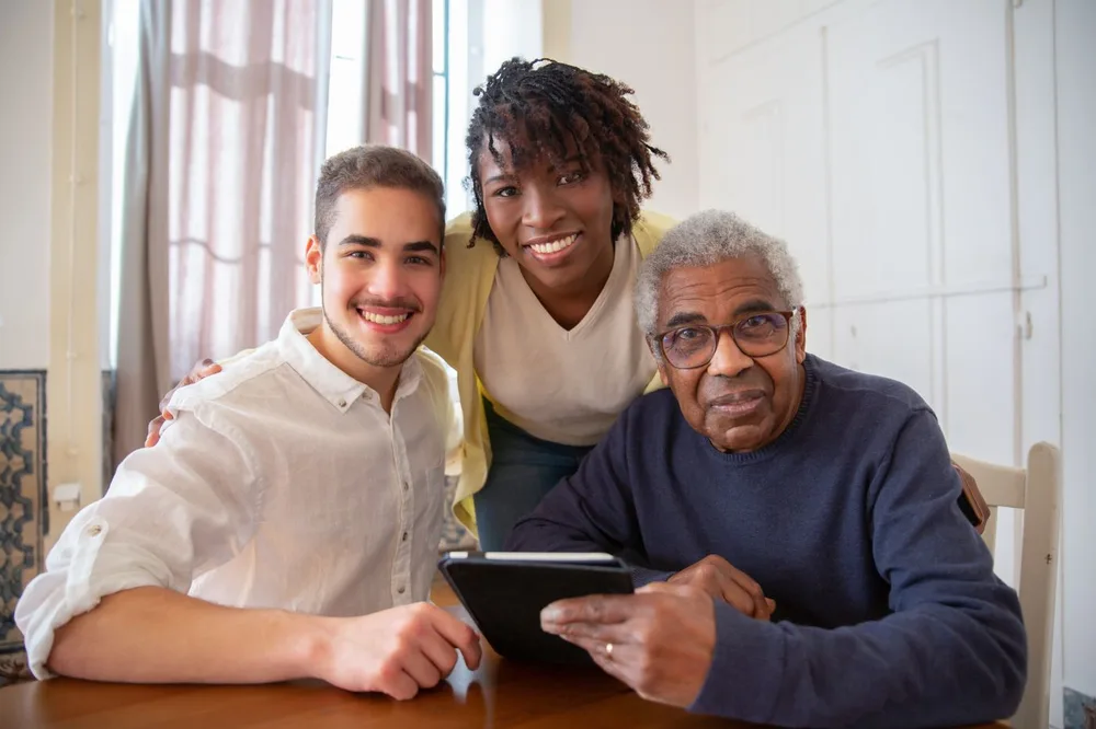 Two adult children smiling with their aging father at home